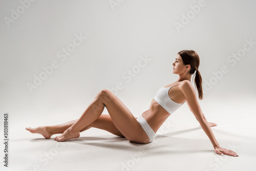 side view of beautiful slim woman in underwear sitting on grey background photo