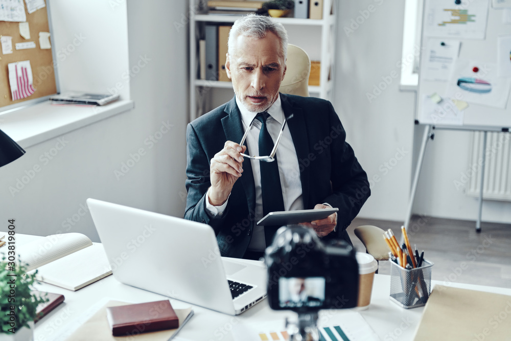 Senior man in elegant business suit using digital tablet while making social media video