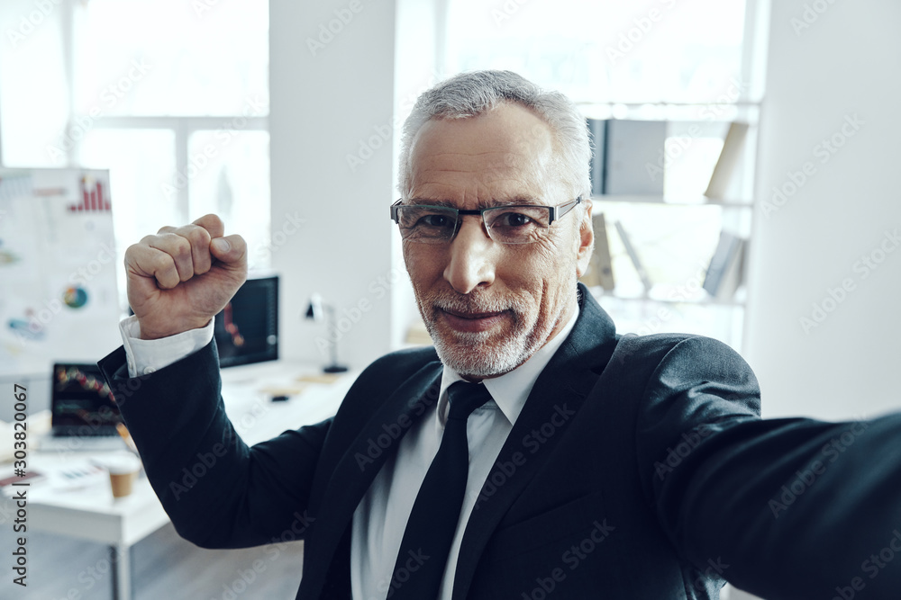 Self portrait of senior man in elegant business suit looking at camera and smiling while standing in office Self portrait of senior man in elegant business suit looking at camera and smiling while standing in office