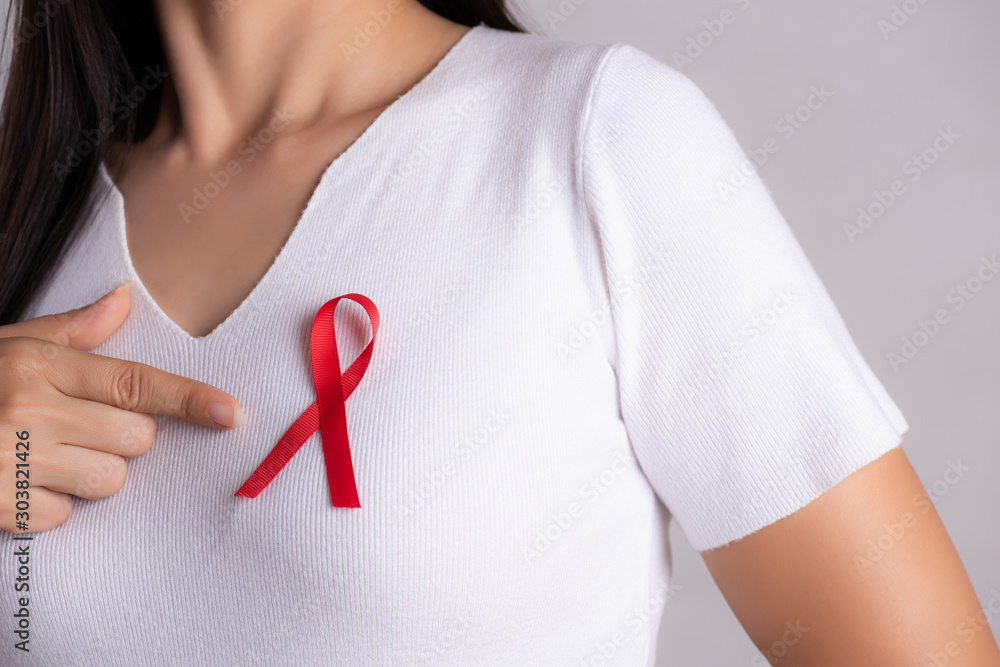 Closeup of woman hand pointing to red badge ribbon on chest to support AIDS Day. Healthcare, medicine and AIDS awareness concept. Closeup of woman hand pointing to red badge ribbon on chest to support AIDS Day. Healthcare, medicine and AIDS awareness concept.