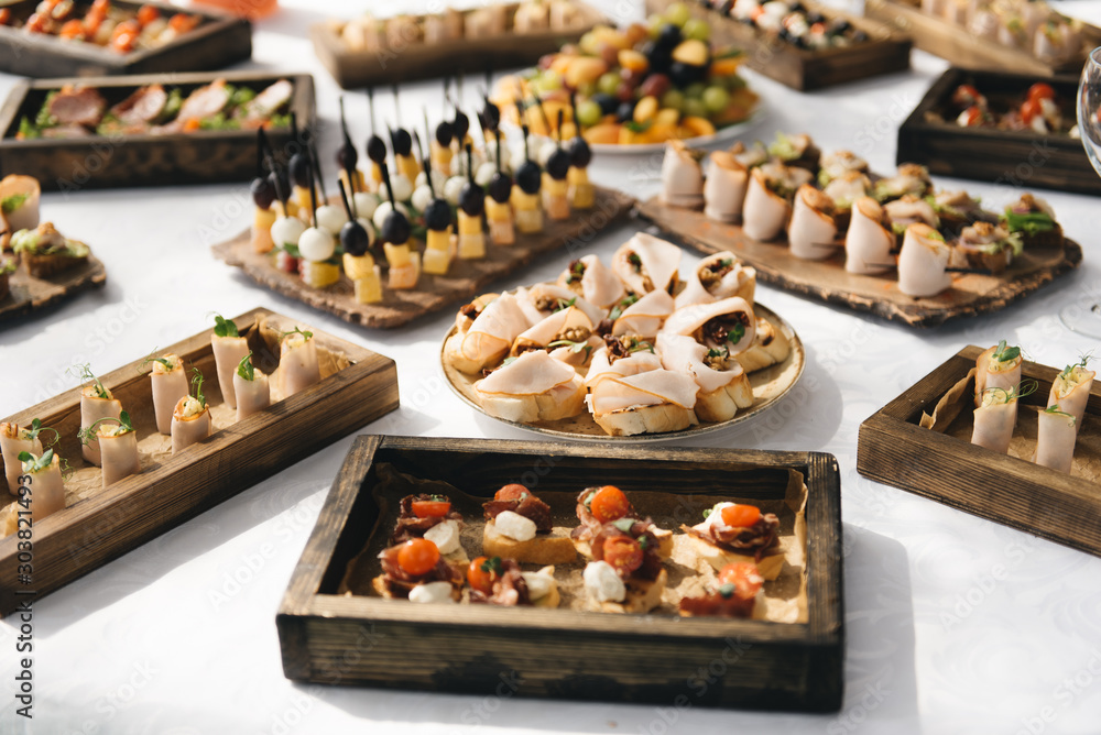 the buffet at the reception. Assortment of canapes on wooden board. Banquet service. catering food, snacks with cheese, jamon, prosciutto and fruit