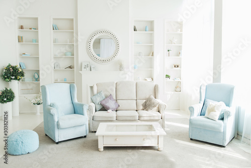 The interior of the modern living room with a white sofa, blue armchairs and a bookshelf at the back