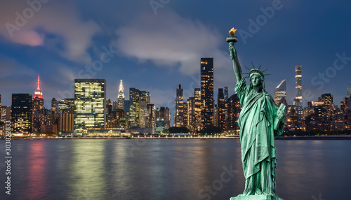 statue of liberty in front of Manhattan skyline at night