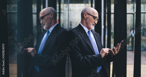 Confident senior businessman in suit and eyeglasses surfing tablet on street