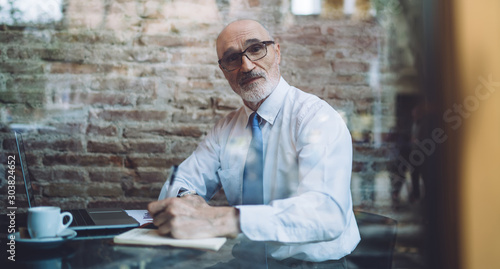 Mature man browsing laptop taking notes at cafe