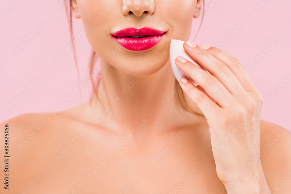cropped view of naked beautiful woman with pink lips holding makeup sponge isolated on pink cropped view of naked beautiful woman with pink lips holding makeup sponge isolated on pink