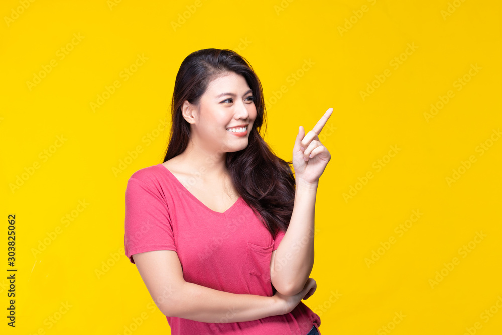 Image of feeling smile and happy. Cheerful young asian woman with brunette long hair in casual shirt smiling with teeth pointing up with index finger to copy space. Female face expressions concept. Image of feeling smile and happy. Cheerful young asian woman with brunette long hair in casual shirt smiling with teeth pointing up with index finger to copy space. Female face expressions concept.