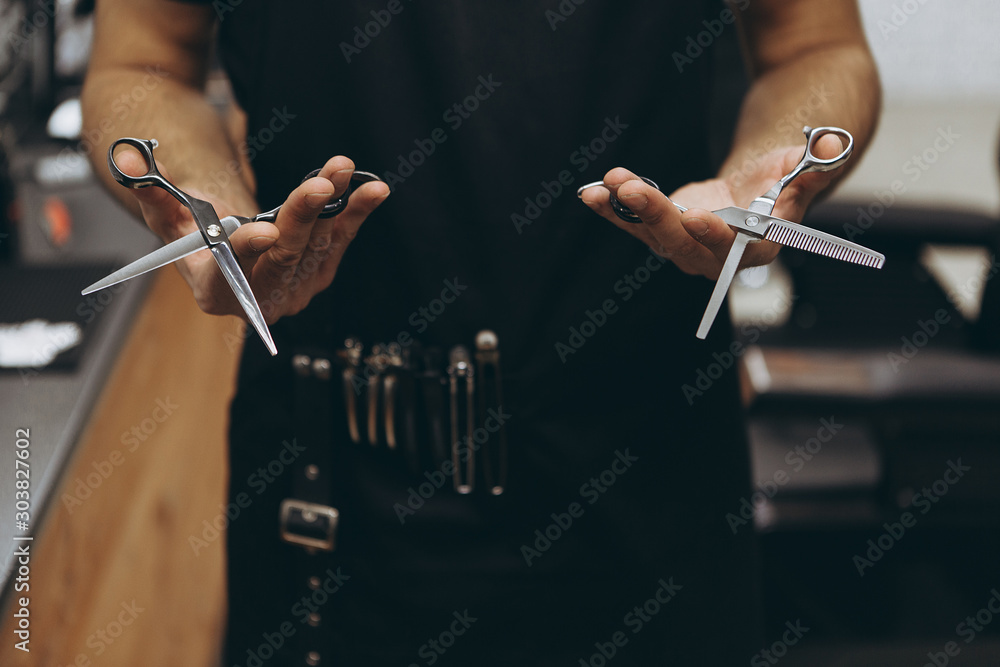 Φωτογραφία Professional hairdresser prepares for a haircut, checks his tool, examines scissors holding them in his hands, focus on scissors
