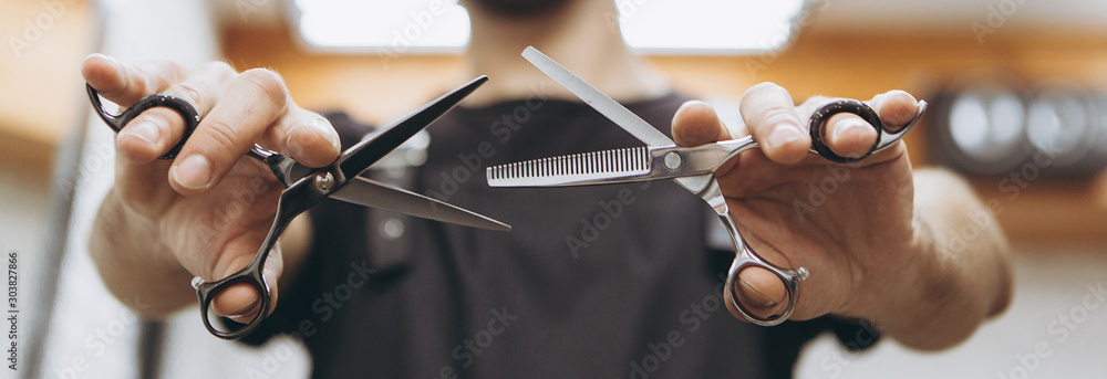 Φωτογραφία Professional hairdresser prepares for a haircut, checks his tool, examines scissors holding them in his hands, focus on scissors