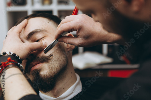 stylish attractive man with a beard in a barbershop. Shaving and modeling a contemporary beard shape in retro style, the barber shaves his client