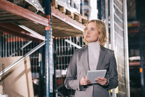 confident businesswoman holding digital tablet while looking away in warehouse photo