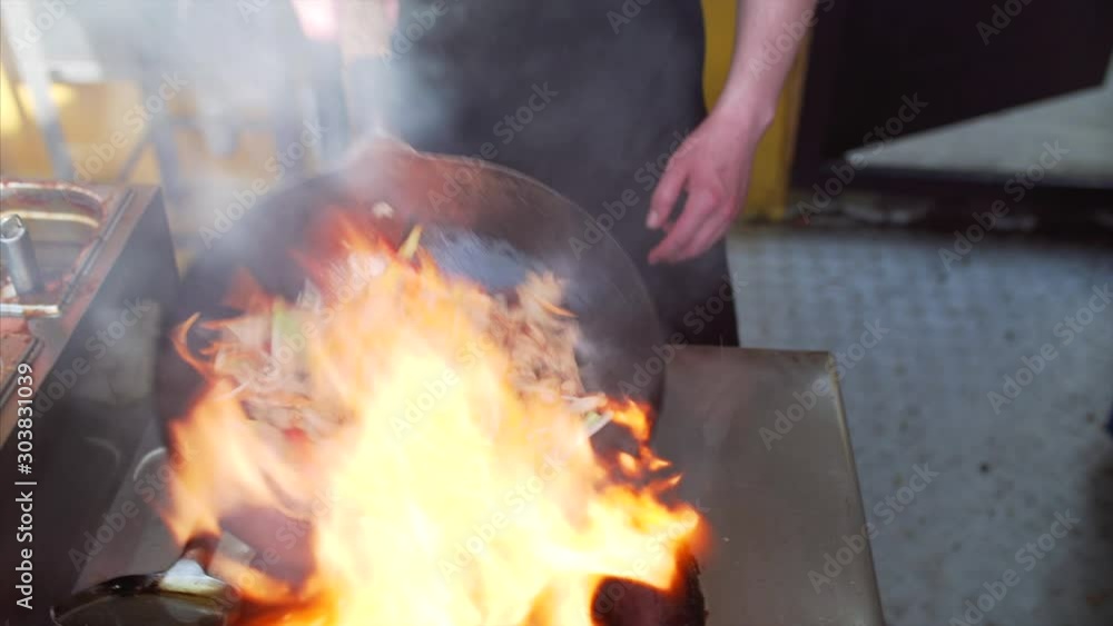 Unidentified chief is cooking wok vegetables and chicken with fire in restaurant Unidentified chief is cooking wok vegetables and chicken with fire in restaurant