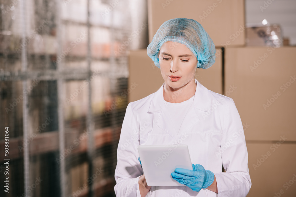 Ταπετσαρία concentrated storekeeper in hairnet using digital tablet in warehouse
