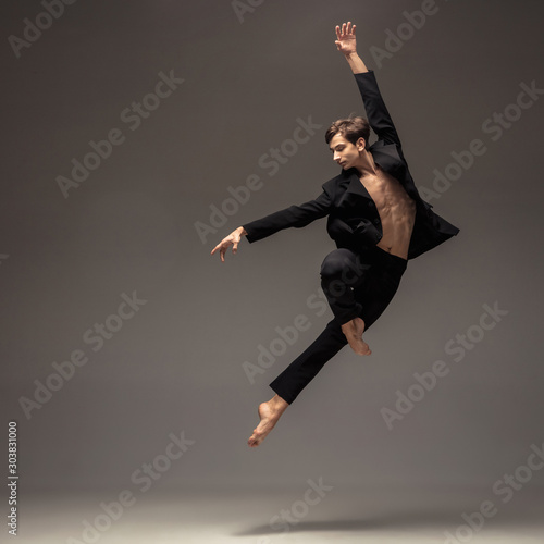 Man in casual office style clothes jumping and dancing isolated on grey background. Art, motion, action, flexibility, inspiration concept. Flexible caucasian ballet dancer, weightless jumps. photo