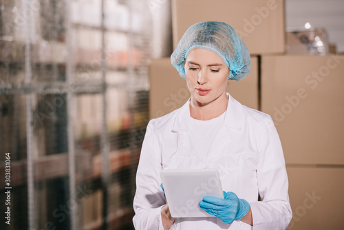 concentrated storekeeper in hairnet using digital tablet in warehouse photo