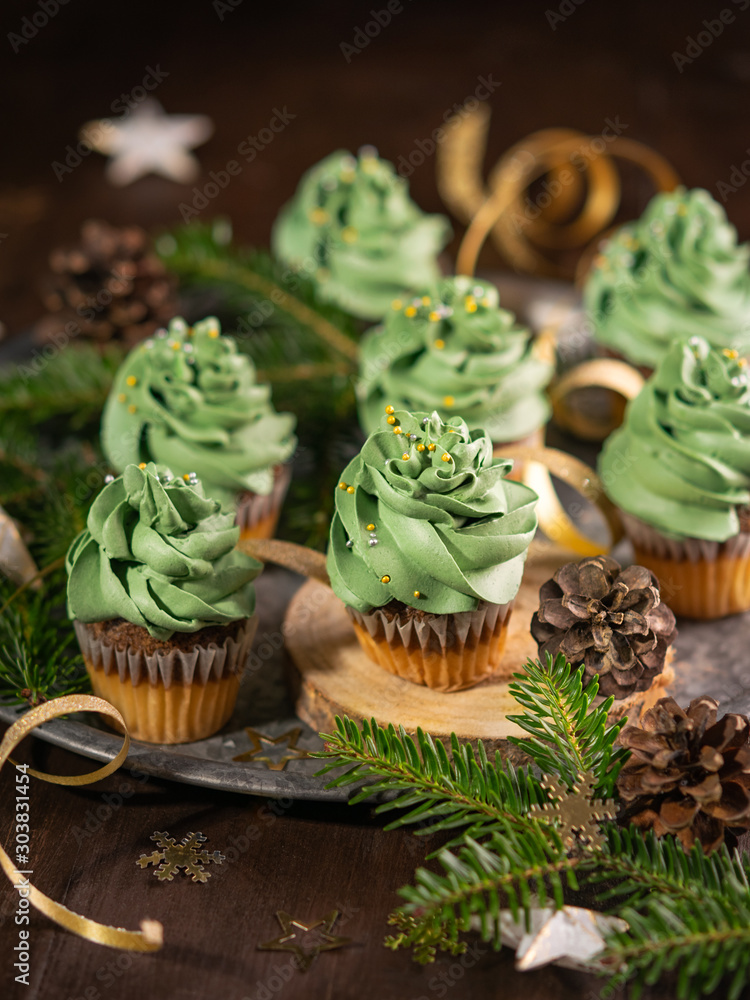Christmas tree cupcakes sweet dessert with golden sprinkles on wooden background with garland lights bokeh. Closeup. Christmas and new year holidays background concept.