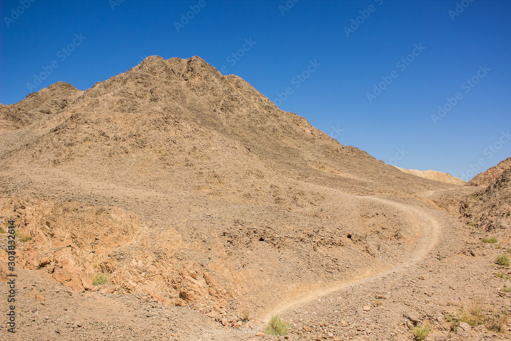 desert mountain landscape photography in clear weather day time with sand stone rocks and lonely dirt trail 