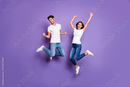 Full length body size photo of cheerful excited positive ecstatic jumping people in jeans denim white t-shit footwear expressing emotions isolated pastel violet color background