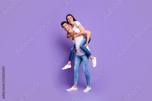 Turned full length body size photo of cute couple of two beloved people piggyback in white t-shirt smiling toothily with man carrying his woman isolated violet pastel color background
