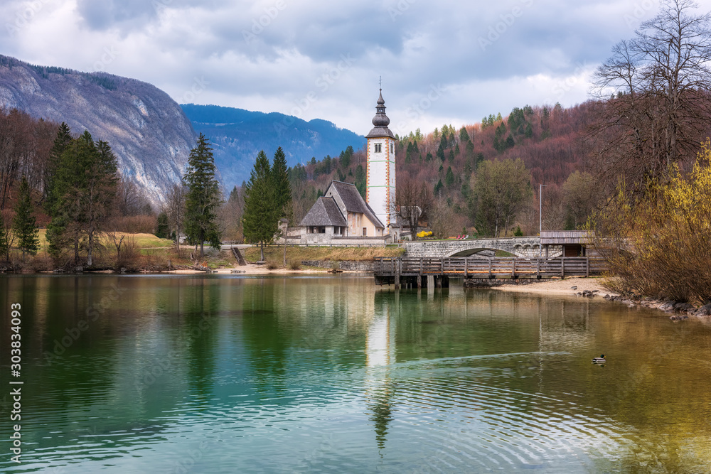 Panoramic spring view of Bohinj lake with the church of St John the Baptist and the stone bridge in Triglav National Park, located in Julian Alps, Slovenia.