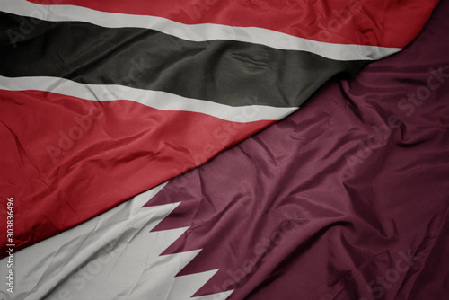 waving colorful flag of qatar and national flag of trinidad and tobago.