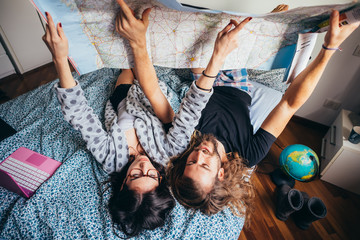 Young couple lying on bed planning travel reading map