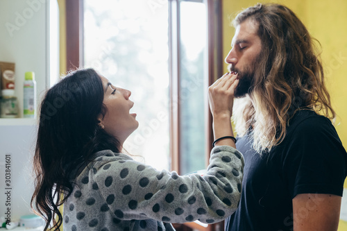 Beautiful woman putting on moisturizer on boyfriend in bathroom at home photo