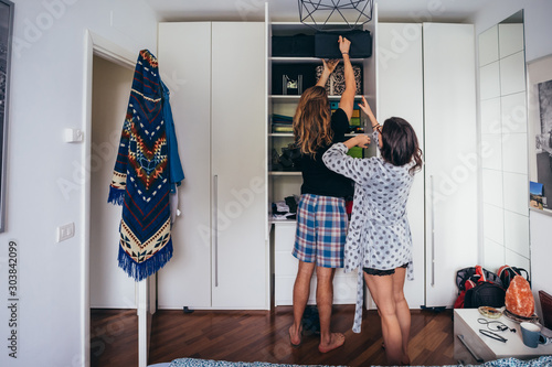 Young beautiful couple indoor bedroom trying to reach the top of the wardrobe photo