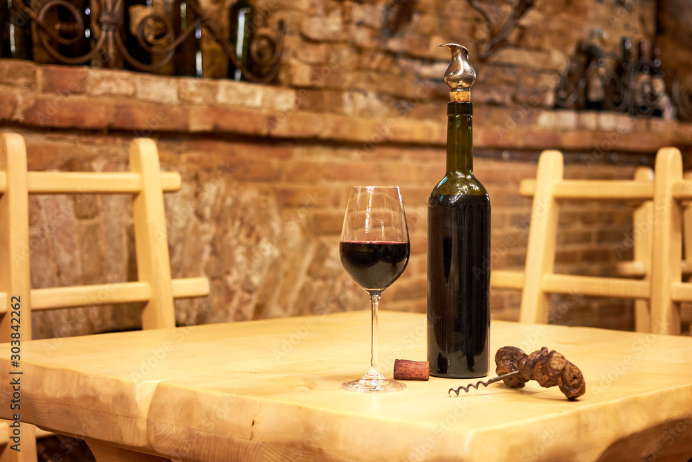 Bottle with red wine and glass with wine on wooden table in the old vintage wine cellar from red brick