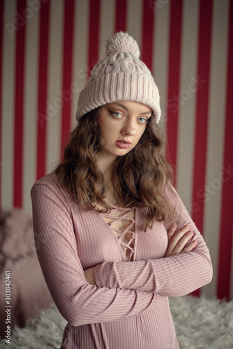 Portrait of cute young woman with blue eyes in a winter warm pink hat waiting for christmas holidays. Peaceful, calm, sad atmosphere.