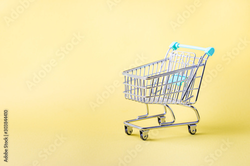 Small empty shopping cart on bright yellow background with copy space
