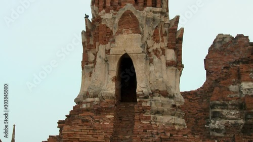 A closeup shot with tilting view of one of Wat Mahathat's Prangs, from its rundown, red brick base to the spire-like tower of gilded bricks and eroded stucco. photo