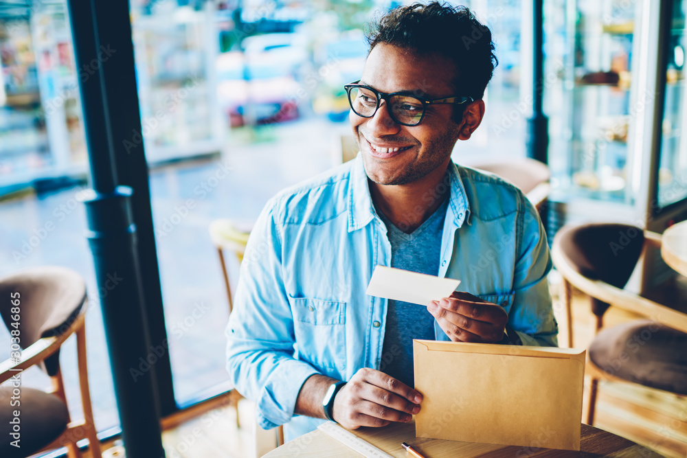 Φωτογραφία Closeup image of handsome smiling hindu male entrepreneur holding small letter from light brown parcel and excited about content