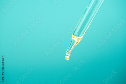 Close-up glass pipette with cosmetic oil essence. Drop yellow serum for skin care on blue background. Concept of natural cosmetic