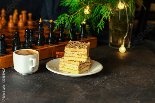 coffee, piece of cake (festive atmosphere, chess, Christmas lights, new year) menu concept. food background. top view. copy space