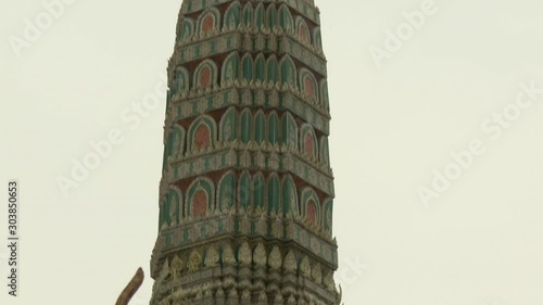 A closeup shot with a tilting view of the richly carved prang of the Prasat Phra Thep Bidon, featuring several metal-scaled chofas at the bottom, in the Wat Phra Si Rattana Satsadaram in Thailand. photo