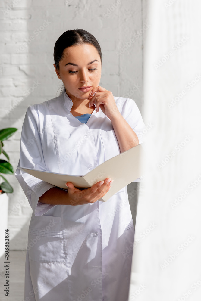 selective focus of attractive dermatologist reading and holding folder in clinic selective focus of attractive dermatologist reading and holding folder in clinic
