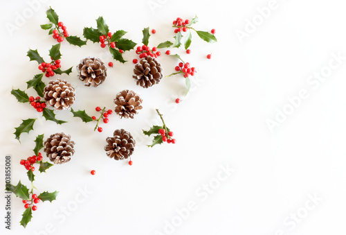 Christmas festive styled floral composition. Pine cones and holly Ilex aquifolium on white table background. Decorative frame, web banner. Flat lay, top view. Copy space.