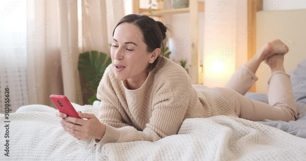 Woman having fun using mobile phone and singing song while relaxing on bed at home Woman having fun using mobile phone and singing song while relaxing on bed at home
