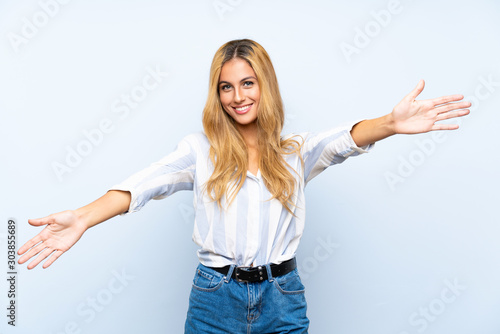 Young blonde woman over isolated blue background presenting and inviting to come with hand