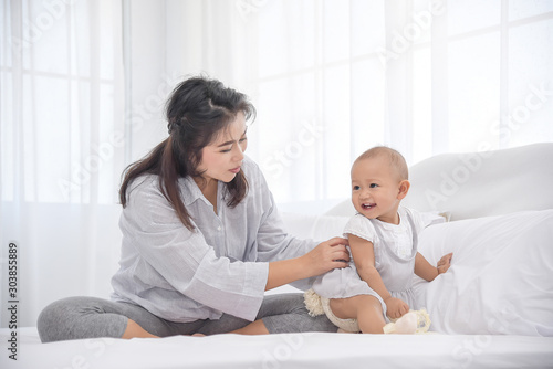 Mother playing with her little infant girl in bedroom. Parent having a happy time together. Happy infant girl smiling to mother.