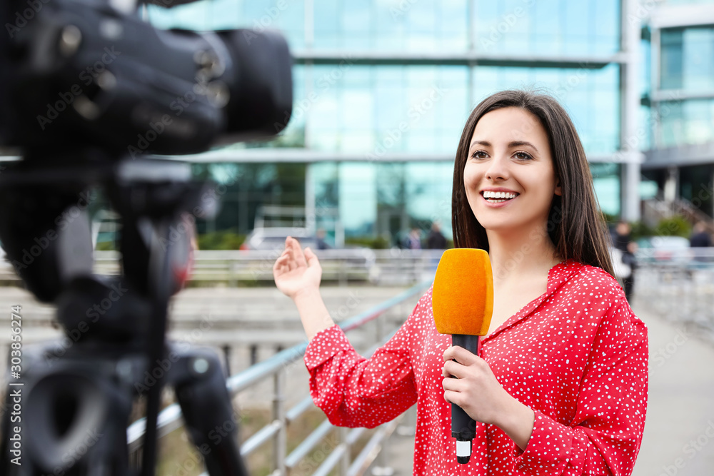 Ταπετσαρία Young female journalist with microphone working on city street