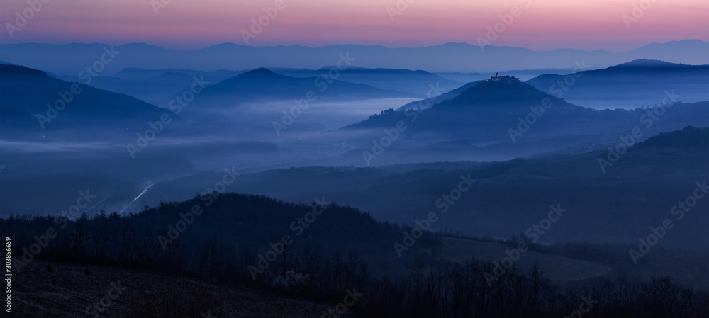 Fototapeta Beautiful scenery of a valley with high mountains enveloped in fog under the breathtaking sunset sky