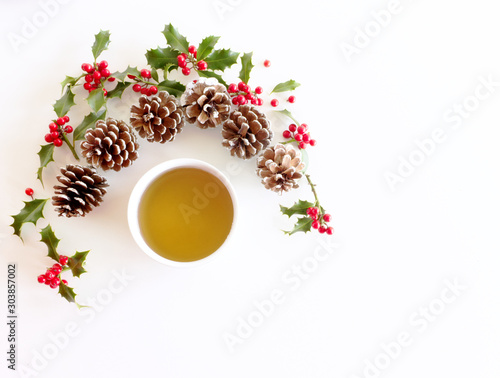 Christmas festive styled floral composition. Pine cones, holly Ilex aquifolium and tea on white table background. Decorative frame, web banner. Flat lay, top view. Copy space.