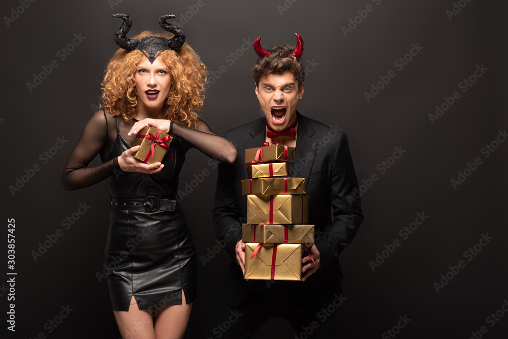 scary couple posing in halloween costumes with gift boxes on black