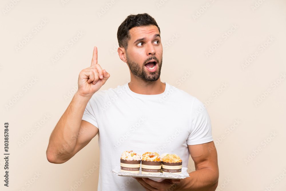 Handsome man holding muffin cake over isolated background intending to realizes the solution while lifting a finger up Handsome man holding muffin cake over isolated background intending to realizes the solution while lifting a finger up