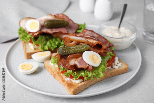 Tasty sandwiches with bacon and quail eggs served on light grey table