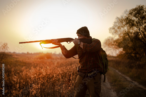 Young irish looking man with a reed, backpack and ammunition belt,  hunting at the countryside near the track in the picturesque sunset rays