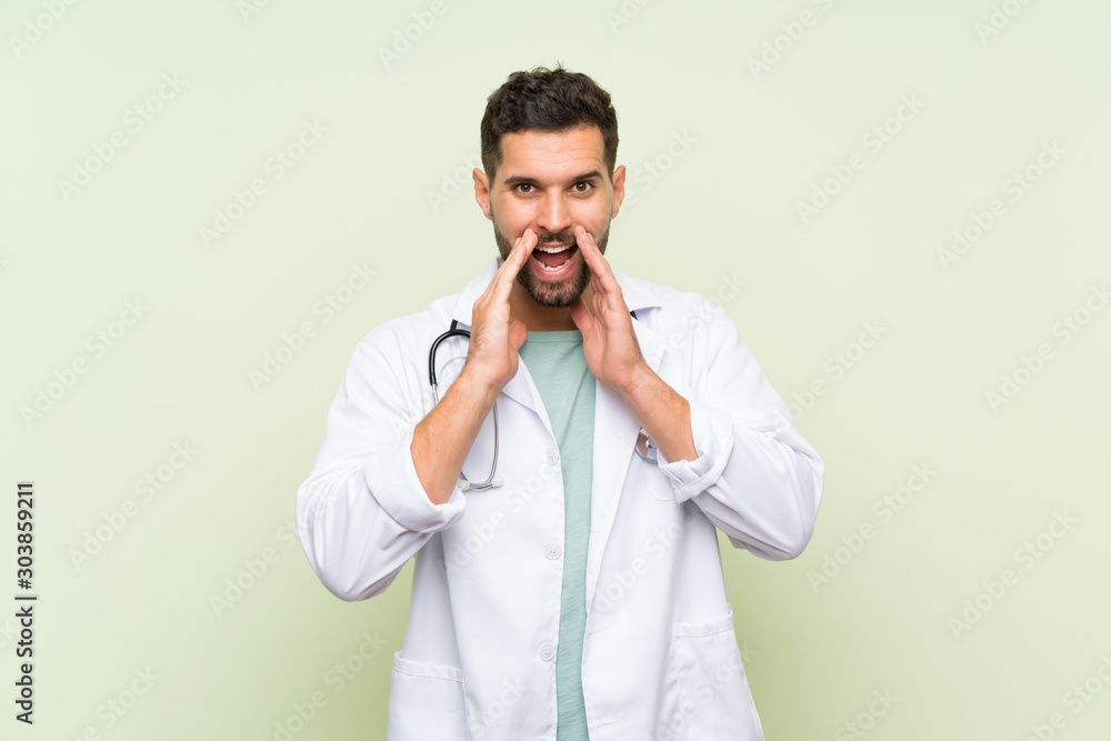 Young doctor man over isolated green wall shouting with mouth wide open Young doctor man over isolated green wall shouting with mouth wide open