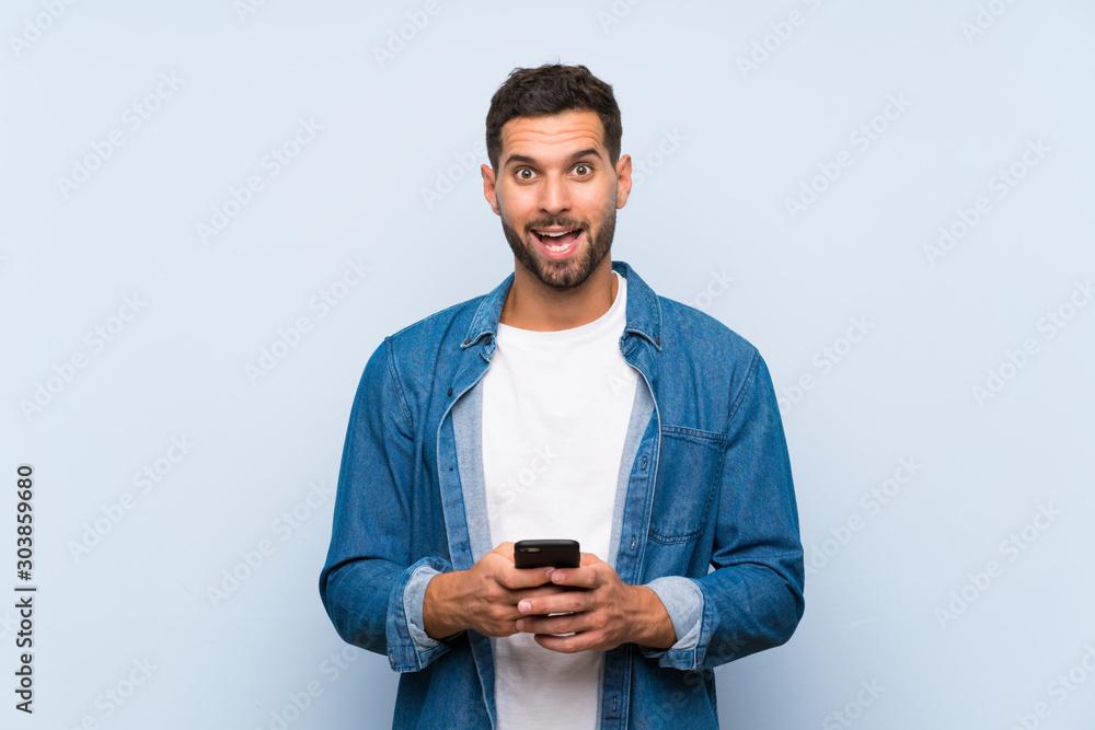 Handsome man over isolated blue background surprised and sending a message Handsome man over isolated blue background surprised and sending a message